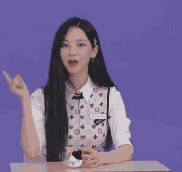 a woman with long black hair is sitting at a table with a louis vuitton vest