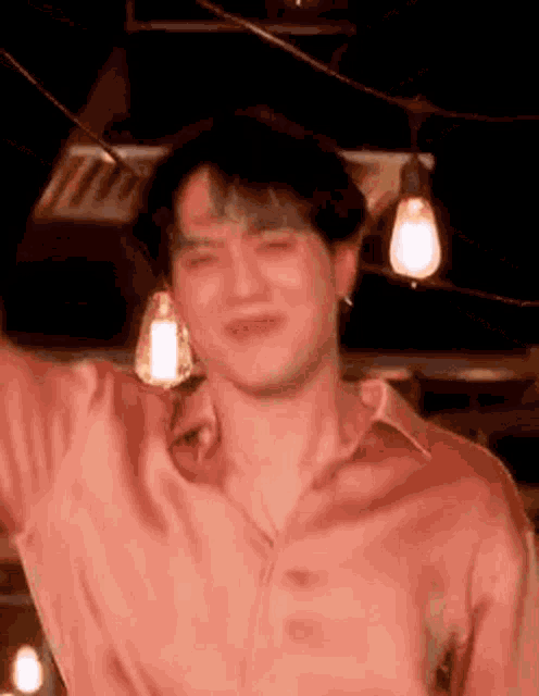 a man in a pink shirt is standing in front of a string of light bulbs .