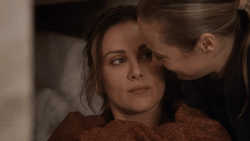 a woman kisses another woman 's forehead while laying in bed