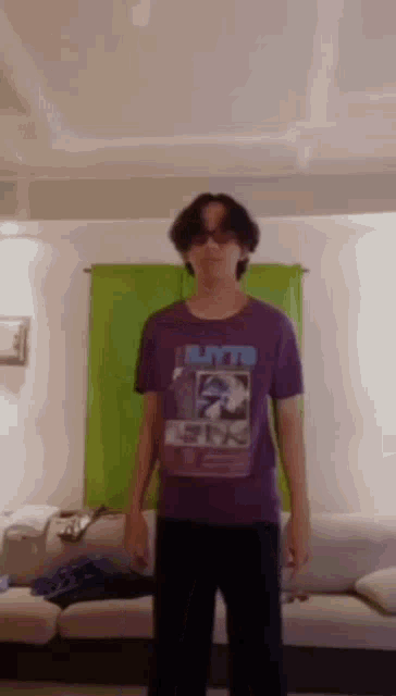 a young man in a purple shirt is standing in front of a couch in a living room .