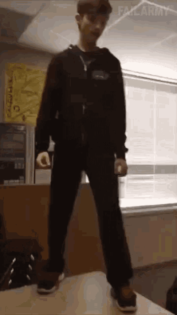a boy is standing on top of a table in front of a window with a failarmy sign behind him