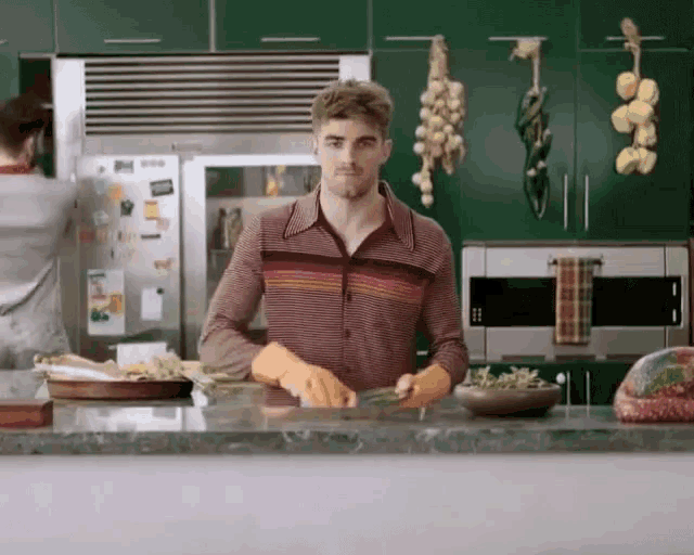 a man wearing orange rubber gloves is standing in a kitchen preparing food