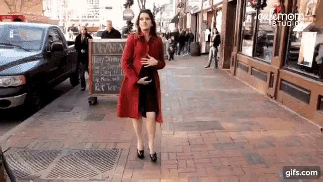 a woman in a red coat is walking down a sidewalk next to a sign that says " i want "