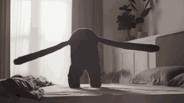a stuffed animal with long arms is standing on a bed in a bedroom