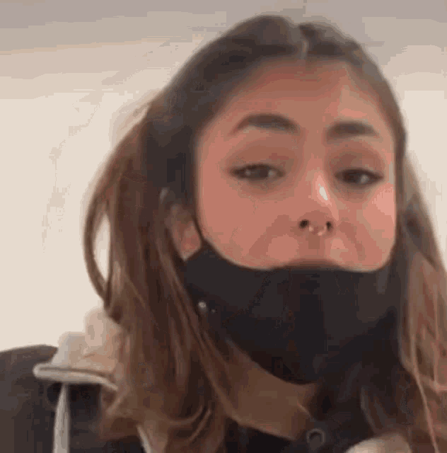 a woman wearing a black face mask and a nose ring is looking at the camera .