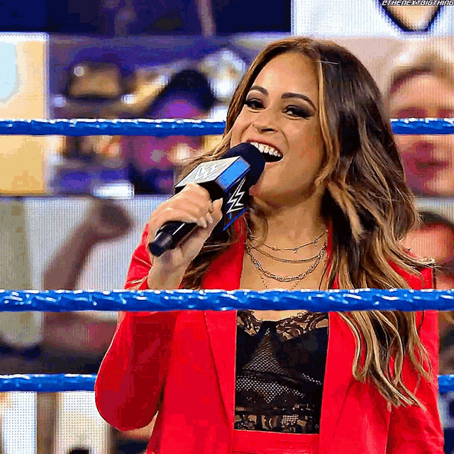 a woman in a red suit is singing into a microphone in a wrestling ring