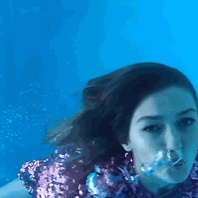 a woman in a purple sequined top is swimming underwater