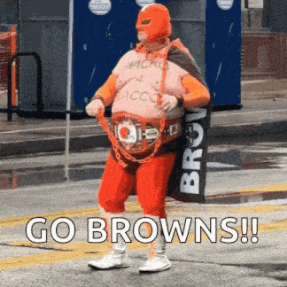 a man in a superhero costume is walking down a street holding a sign that says go browns .