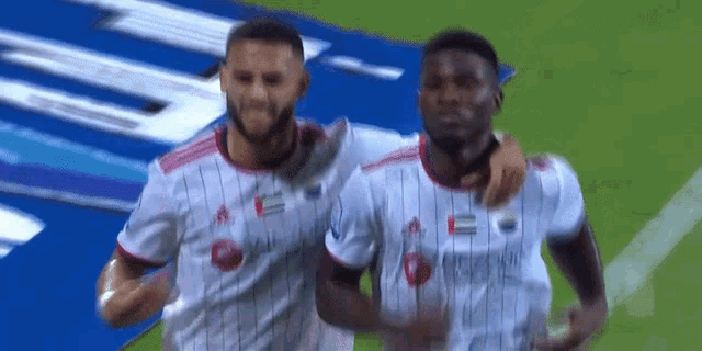 two soccer players are hugging and celebrating a goal on the field .