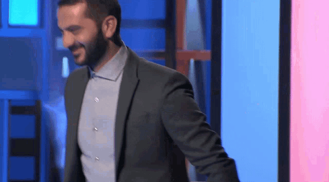 a man in a suit and blue shirt is standing in front of a blue wall