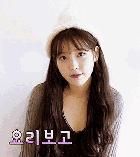 a woman wearing a white hat and a grey sweater has korean writing on the bottom right