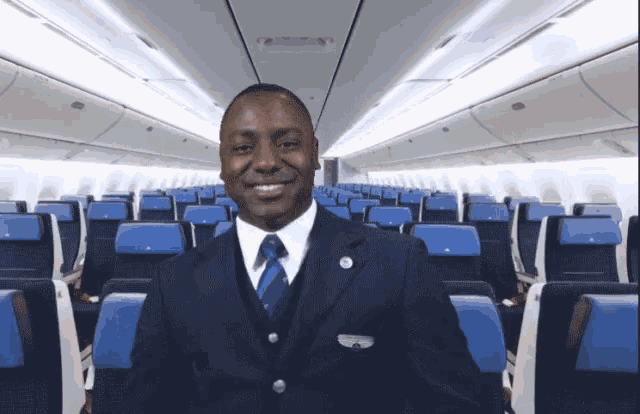a man in a suit and tie stands in an airplane with blue seats