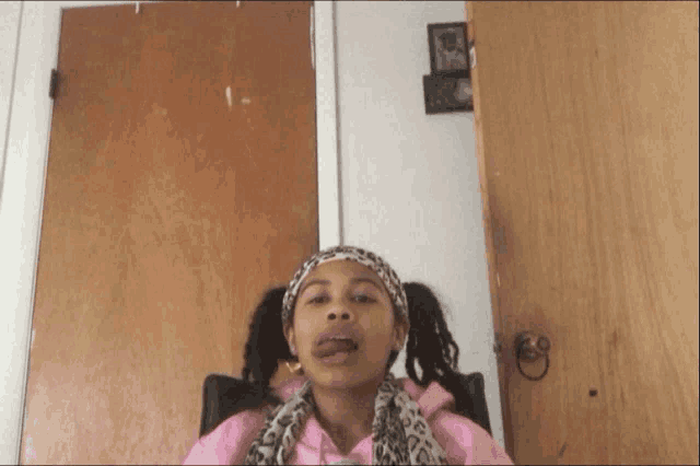 a girl wearing a pink shirt and a leopard print scarf is sitting in front of a wooden door