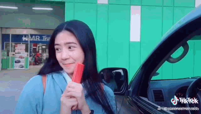 a woman is standing next to a car holding a red object in her hand