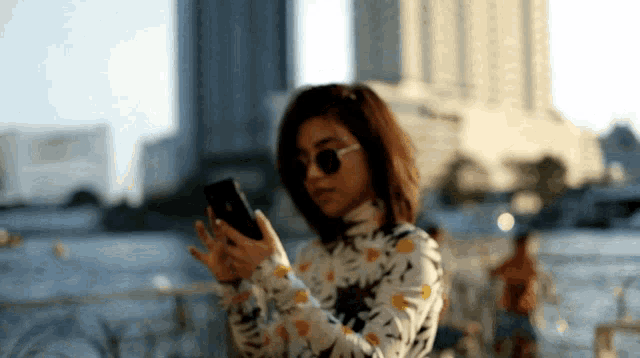 a woman wearing sunglasses and a floral shirt is looking at her phone