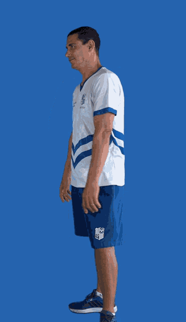 a man with his arms crossed wearing a white shirt and blue shorts with a logo on the shorts