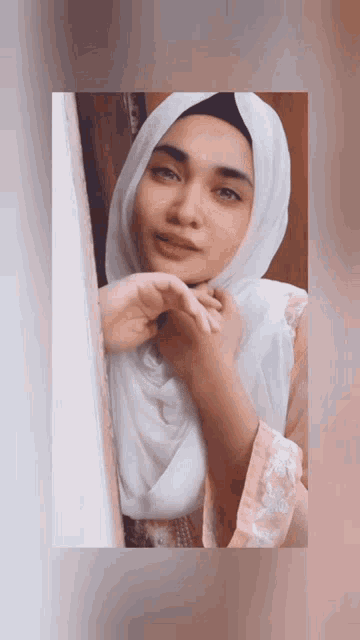 a woman wearing a white hijab and a pink shirt looks at the camera