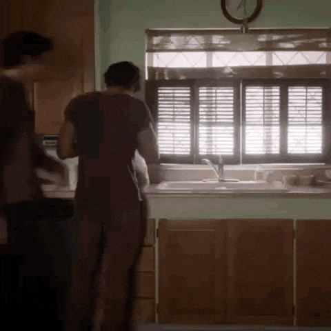 a man and a woman are standing in a kitchen in front of a window .