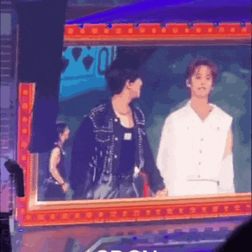 two men are standing next to each other in front of a mirror on a stage .