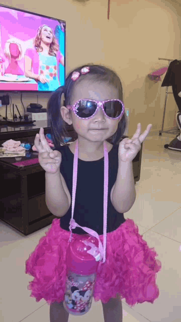 a little girl wearing sunglasses and a minnie mouse water bottle giving a peace sign