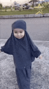 a little girl wearing a hijab and a hat is standing on the ground .