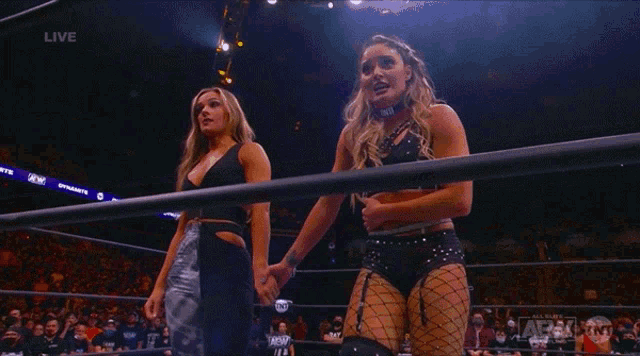 two women are holding hands in a wrestling ring with a state farm banner behind them
