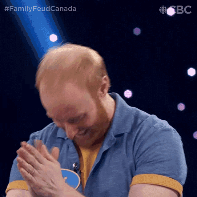 a man in a blue shirt is clapping his hands in front of a spotlight that says #familyfeud canada