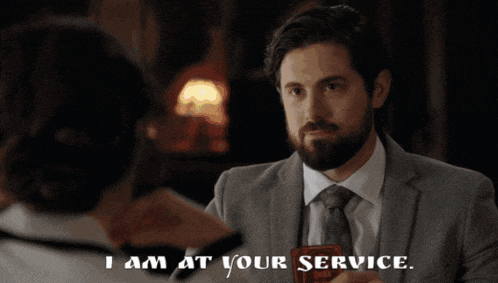 a man in a suit and tie is talking to a woman who says " i am at your service "