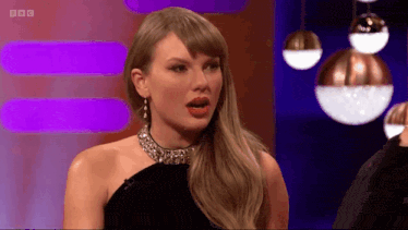 a woman in a black dress with a choker and earrings is on a stage with a bbc logo in the corner