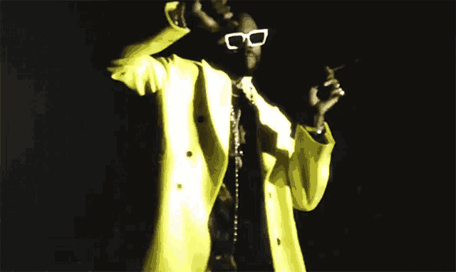 a man wearing sunglasses and a yellow coat holds a microphone in his hand