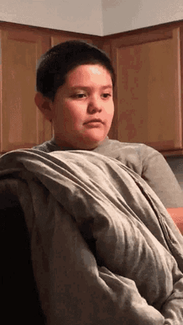 a young boy is wrapped in a blanket and looking at something