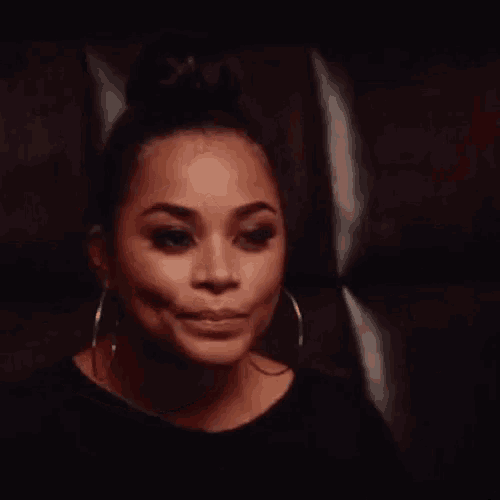 a woman wearing hoop earrings and a black shirt is standing in front of a wall .
