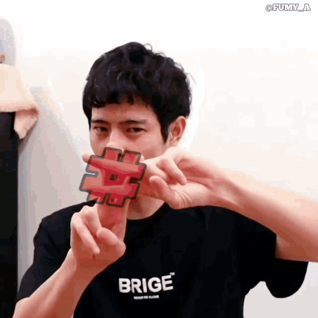 a man wearing a brige t-shirt holds a red hashtag