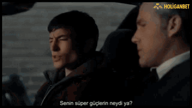 two men are sitting in a car with the word holiganbet on the bottom