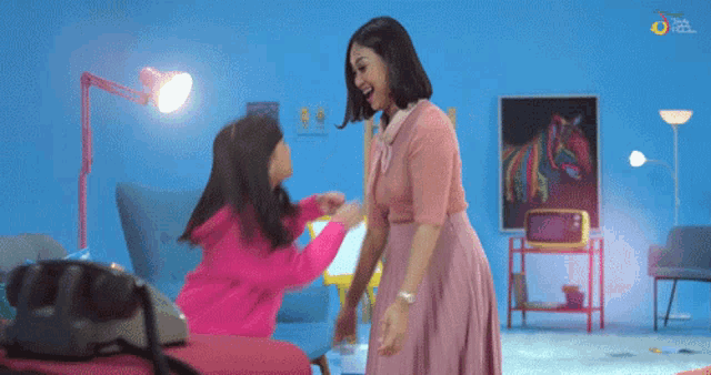 a woman in a pink dress is standing next to a little girl in a living room