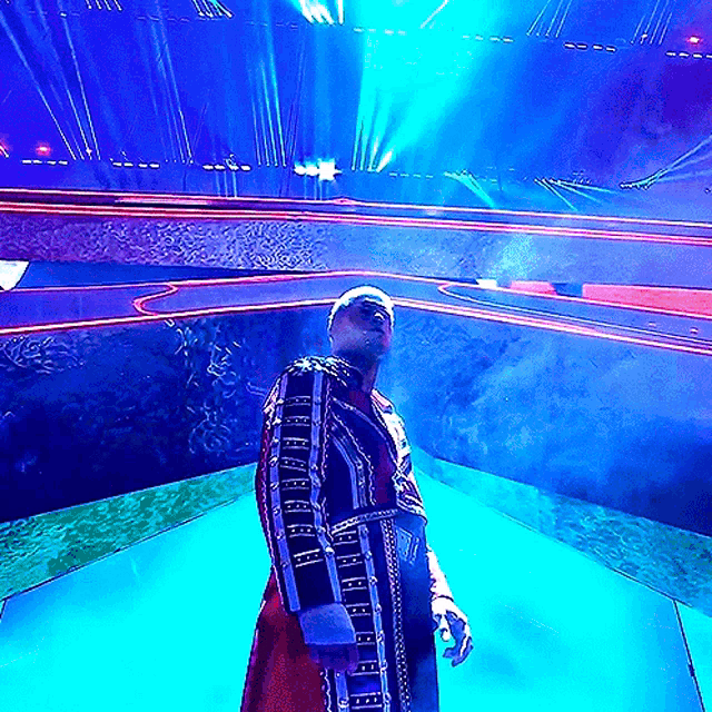 a man in a robe stands in front of a stage with blue lights