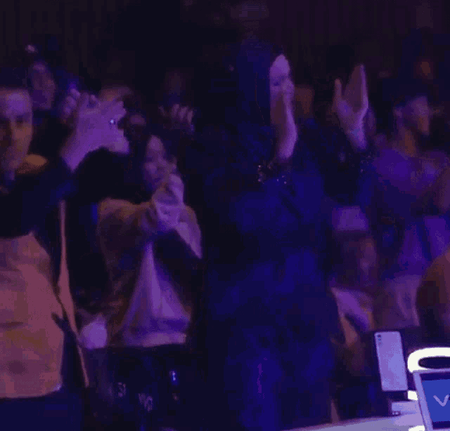a woman in a hijab is applauding in front of a crowd of people .