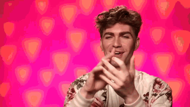 a young man in a floral shirt is making a heart shape with his hands .