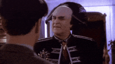 a bald man is sitting in a chair and talking to another man