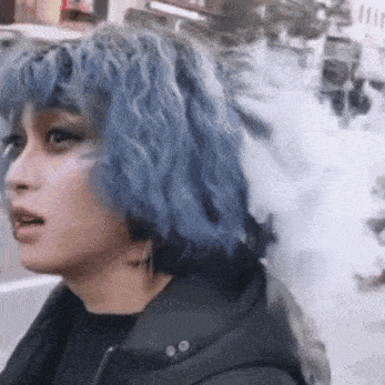 a woman with blue hair and smoke coming out of her mouth is walking down a street .