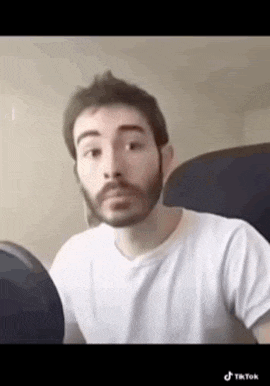 a man with a beard wearing a white shirt is sitting in a chair .