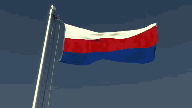 a red white and blue flag is waving in the wind against a blue sky