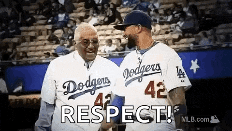 two men wearing dodgers jerseys are standing next to each other on a baseball field and shaking hands .