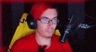 a man with red hair and glasses is sitting in front of a microphone wearing headphones .