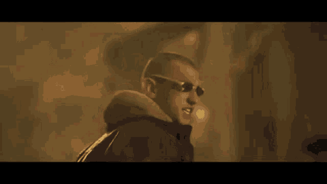 a man wearing sunglasses and a hooded jacket is standing in the dark .