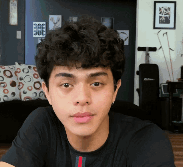 a young man with curly hair wears a black shirt with a green and red stripe