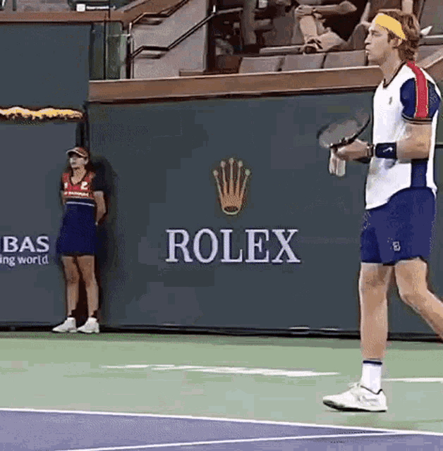 a man is holding a tennis racquet on a tennis court in front of a rolex sign