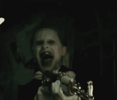 the joker from suicide squad is holding a gun in his hand and making a funny face .