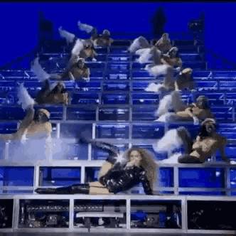 a woman is laying on a stage with a bunch of people behind her .