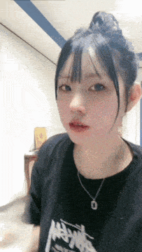 a girl wearing a black t-shirt with the letter o on it looks at the camera with a necklace around her neck